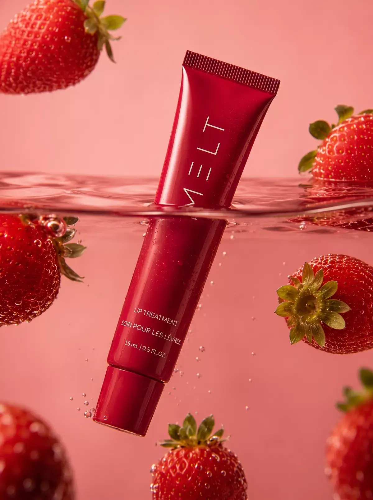 The MELT tube floats half submerged in pink water among strawberries.